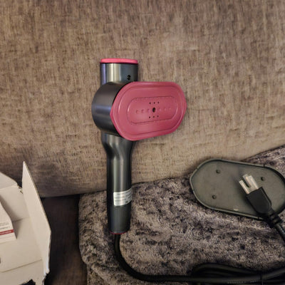CreaseFree steamer with pink press plate resting on a lounge, power cord beside it